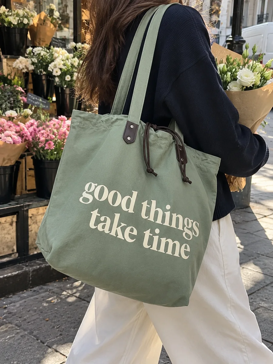 Sage-green bag, cream "good things take time" print, on the shoulder
